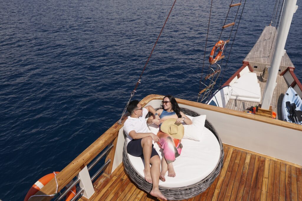 A couple relaxing together on a round daybed on deck above blue water
