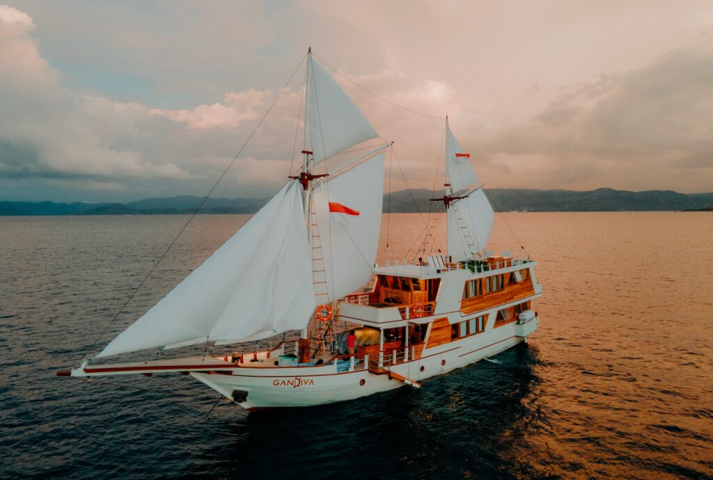 Gandiva phinisi under sail at sunset near Labuan Bajo, dramatic orange sky