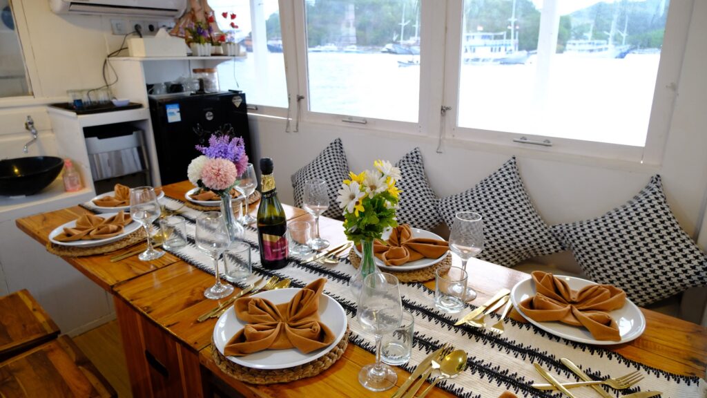 Dining salon table set with gold cutlery, flowers, and a harbor view