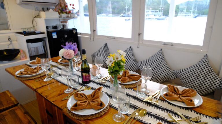 Dining salon table set with gold cutlery, flowers, and a harbor view
