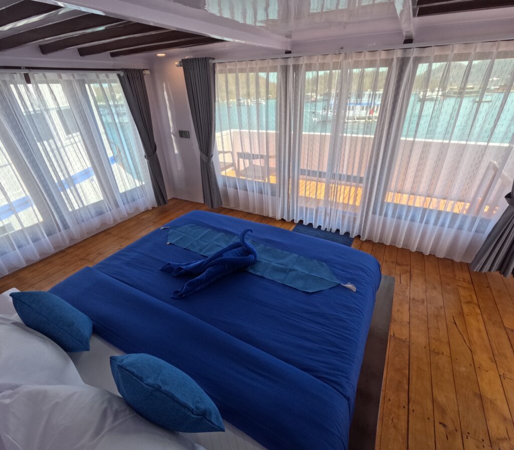 Master cabin with a blue bed facing floor-to-ceiling glass doors to a balcony