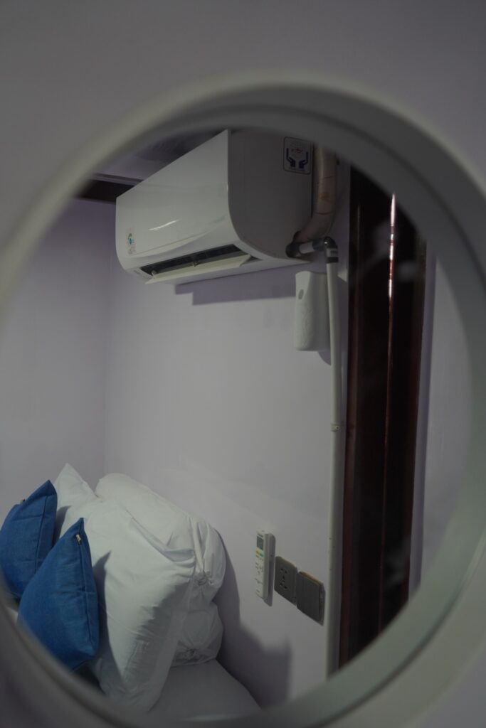 Circular mirror reflecting a bed with blue pillows and an air conditioning unit