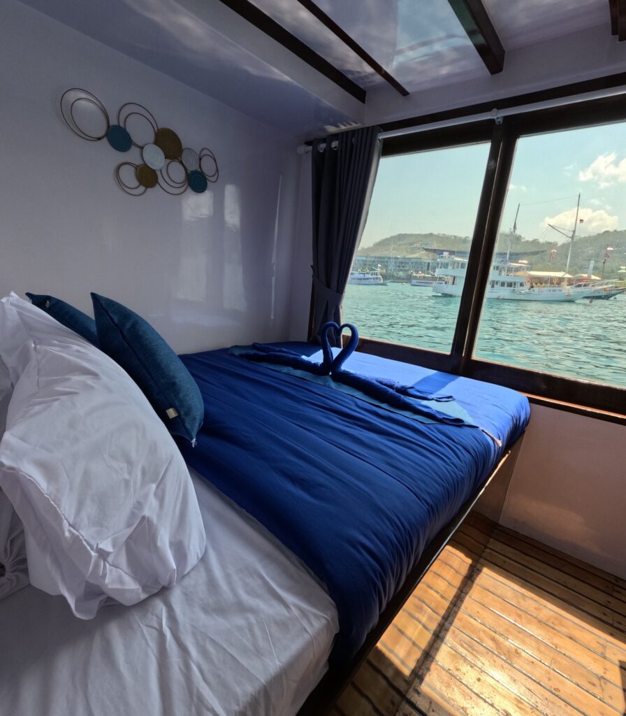 Superior Cabin bed with blue linens on the Invictus, looking out to the harbor