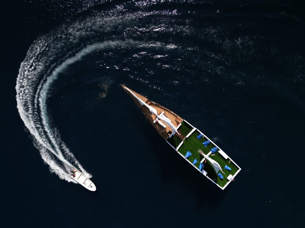 Aerial view of a tender speedboat circling the anchored Invictus, leaving a white wake