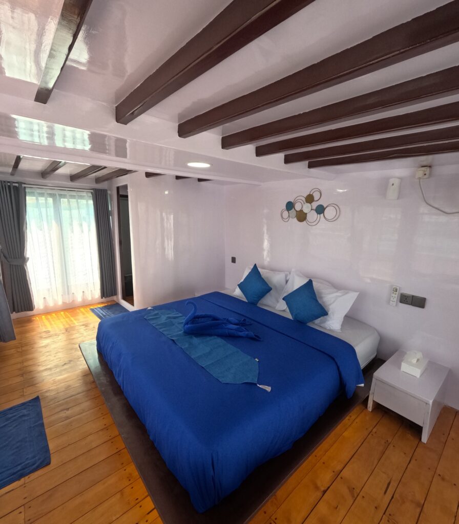 Master stateroom with a blue bed, timber flooring, and wood beam ceiling