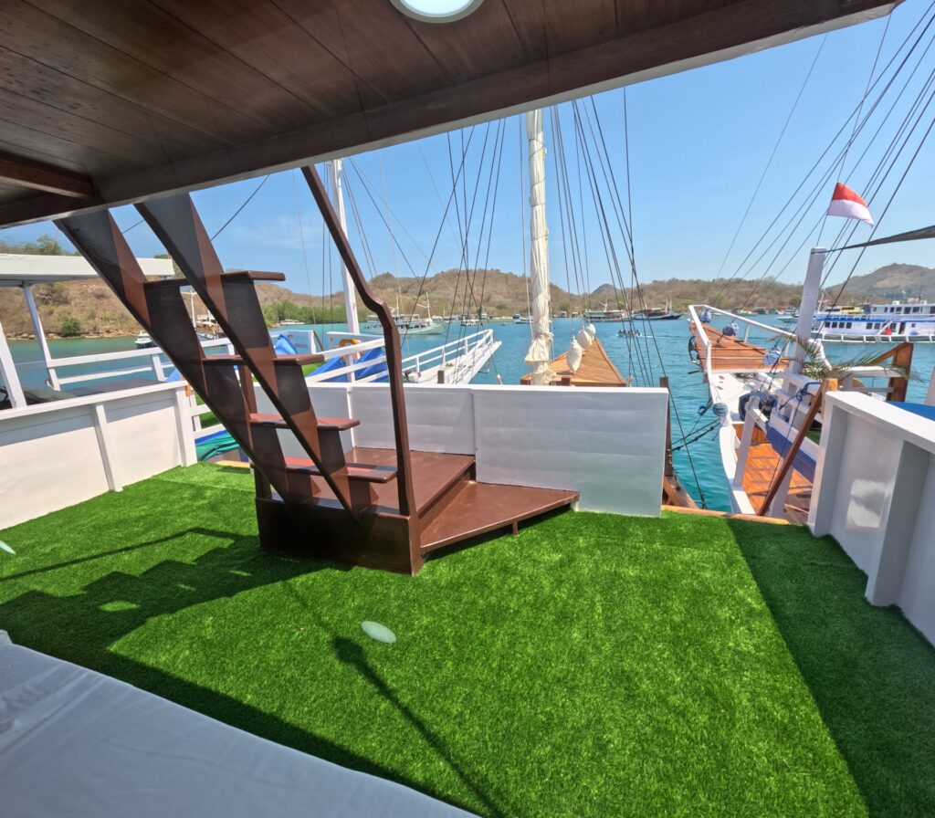 Open upper deck covered in green turf with wooden stairs and harbor views