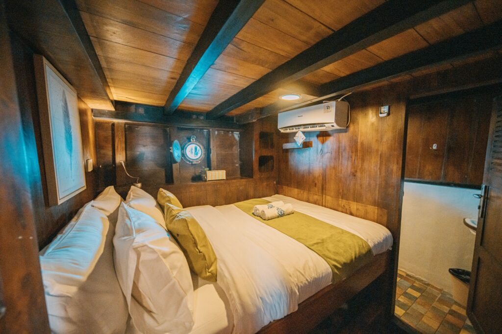 Deluxe lower cabin with a bed in white and olive linens under blue accent light