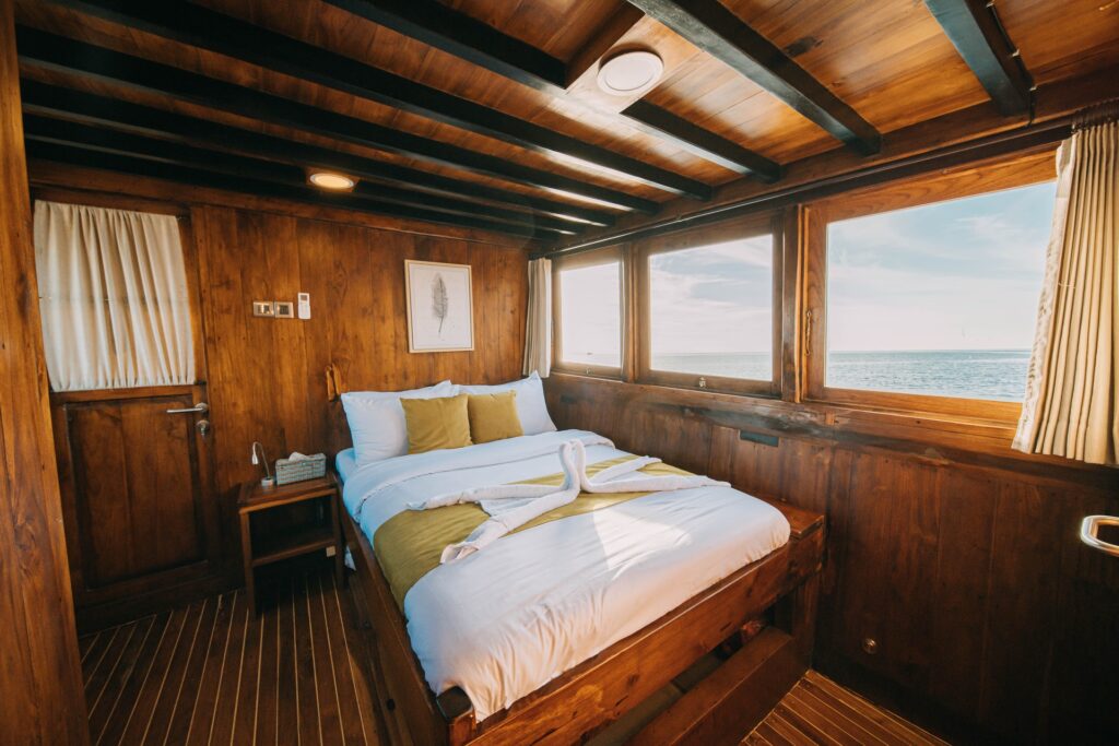Suite aboard the Jofiel with a bed in white and olive linens facing ocean-view windows