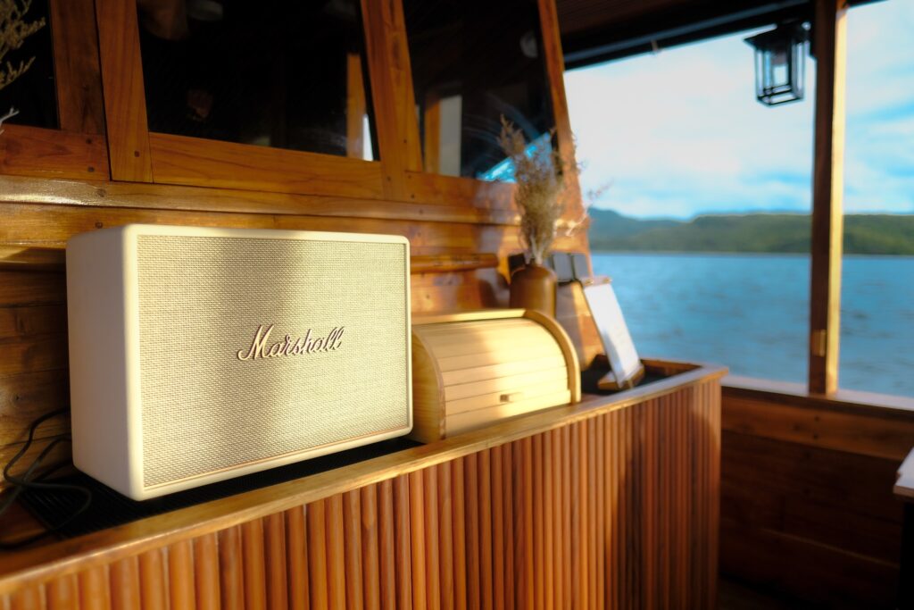 A speaker and lantern on a wooden shelf with a water view behind