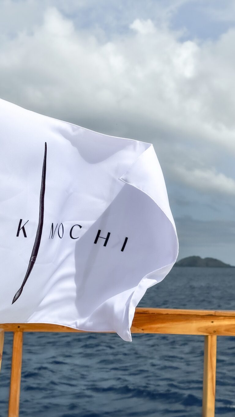 A white Kimochi branded flag waving over the ocean and islands