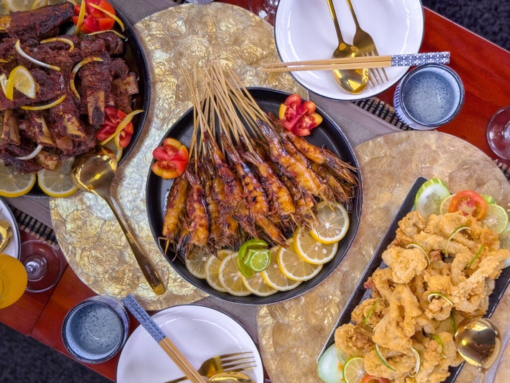 Top-down view of grilled satay skewers, ribs, and fried shrimp
