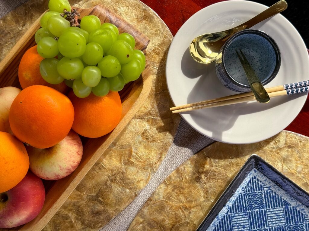 A wooden platter of grapes, oranges, and apples beside a drink and chopsticks