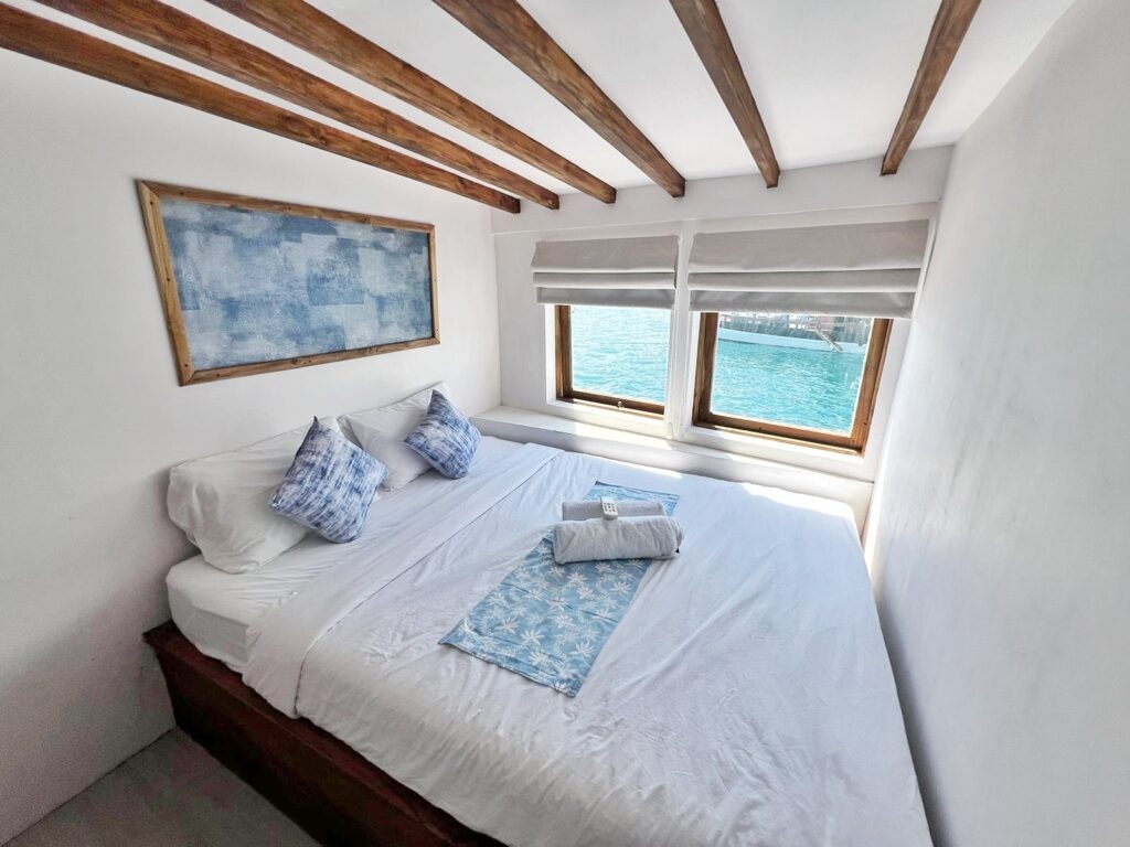 Deluxe cabin bed with blue pillows facing ocean-view windows