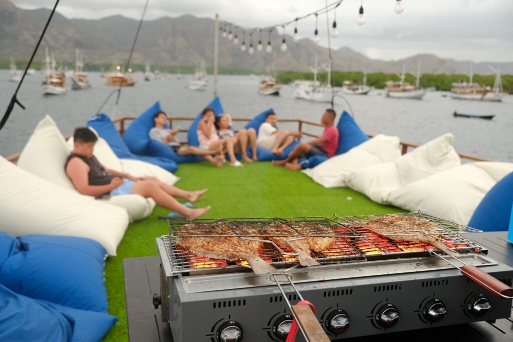 Skewers grilling on a deck barbecue aboard the Leticia with guests seated behind