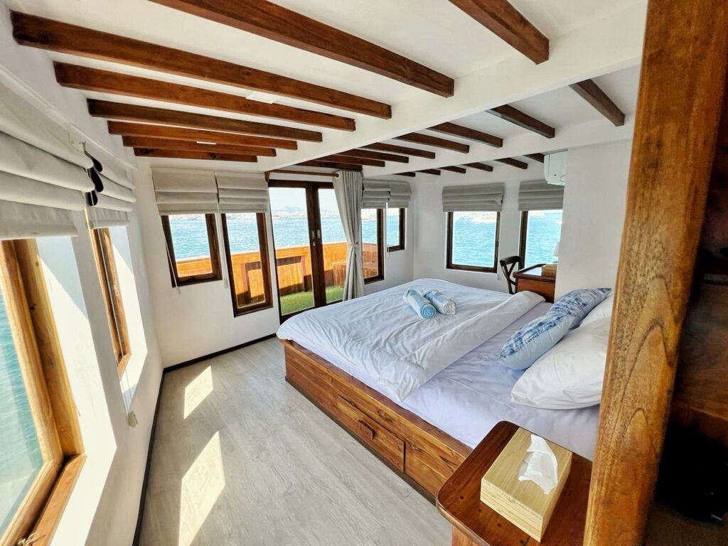 Owners suite with a bed beneath wood beams and wraparound windows