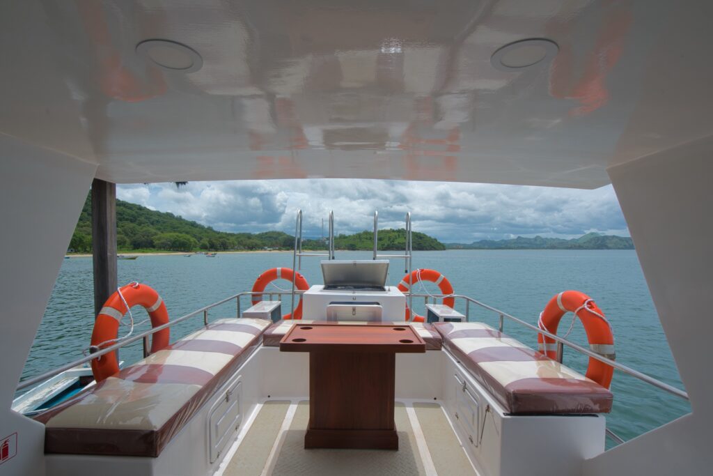 Ocean Queen upper deck lounge with wooden table, bench seating, and lifebuoys