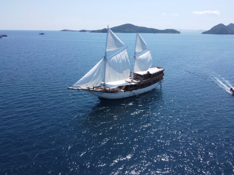Panrita underway with sails raised and a motorboat trailing across open water
