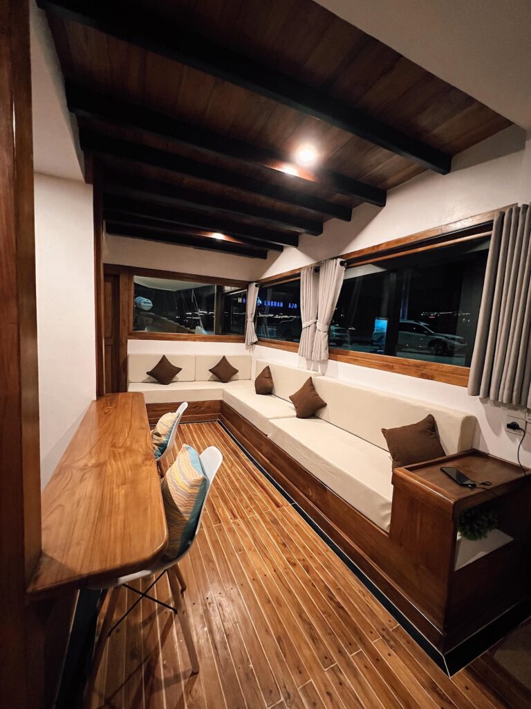 Wood-paneled lounge aboard the Panrita Komodo liveaboard with bench seating and bar table
