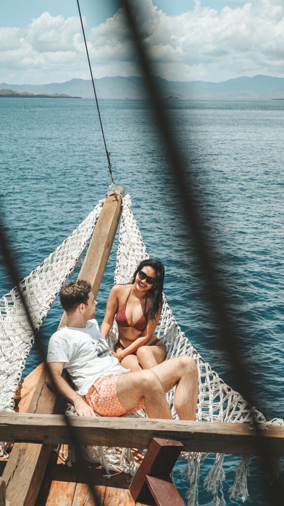 Couple relaxing on the Papiton Duwa phinisi bow net over turquoise water