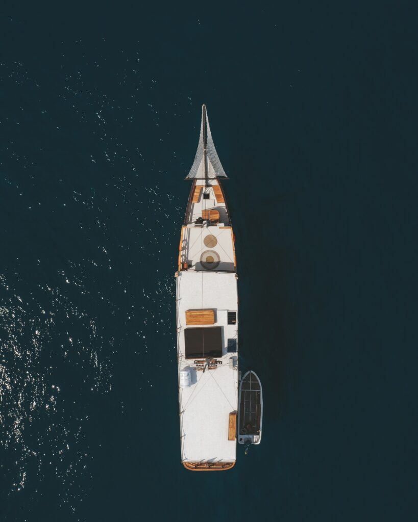 Top-down drone shot of the phinisi anchored in dark blue water with its tender
