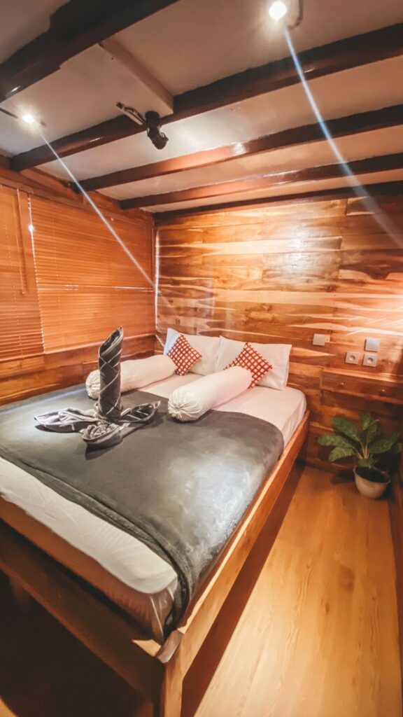 Superior Stateroom bed with folded towel art and red accent pillows against timber walls