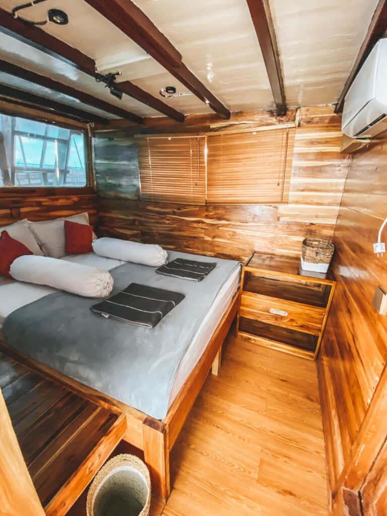 Wood-paneled cabin with a bed, red pillows and a built-in timber nightstand