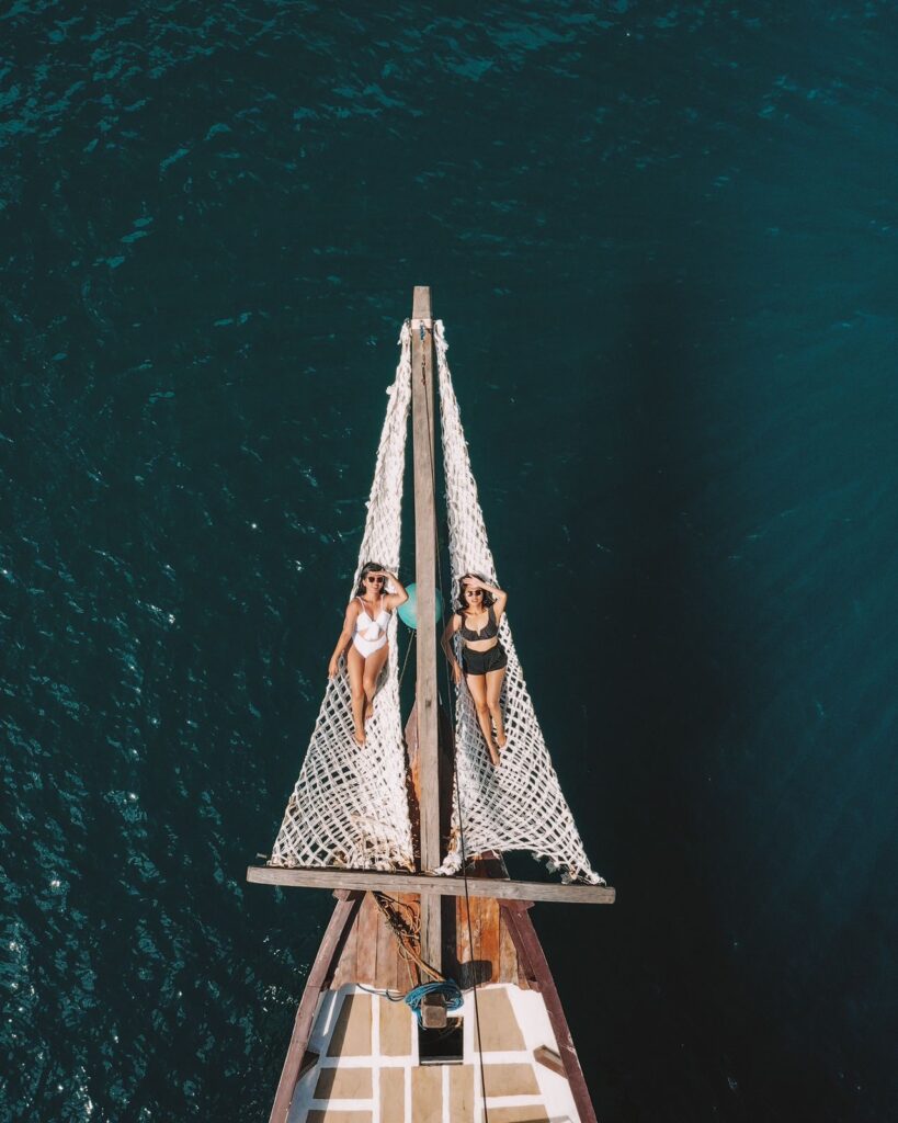 Two guests sunbathing on the dual bow nets above deep blue water