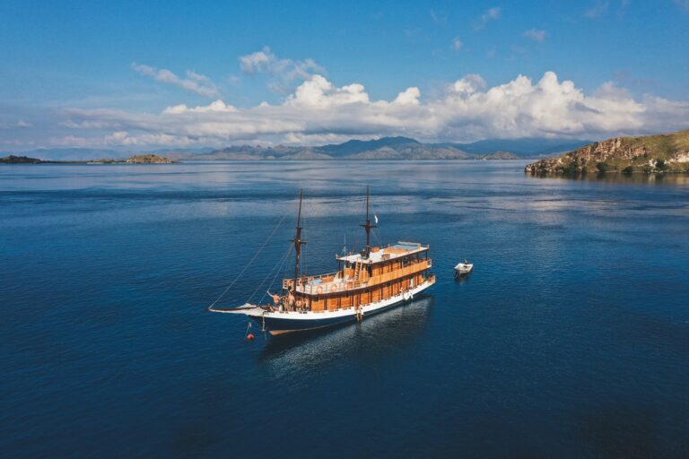 Papiton Lopi komodo liveaboard sailing toward green island hills under a blue sky