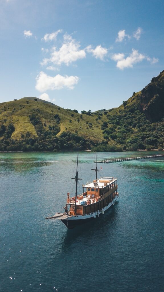 A liveaboard anchored in a shallow turquoise bay near a long wooden pier