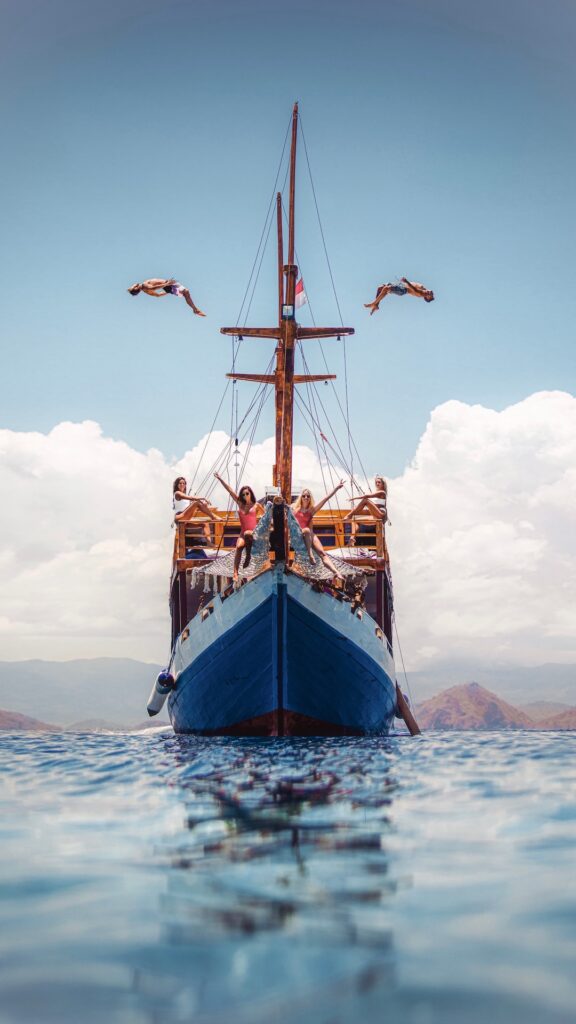 Guests leap off the boat's deck into the air above turquoise water