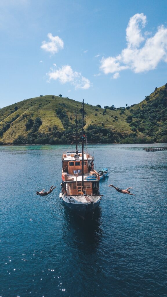 Two swimmers float beside Papiton Lopi anchored in a green-hilled tropical bay