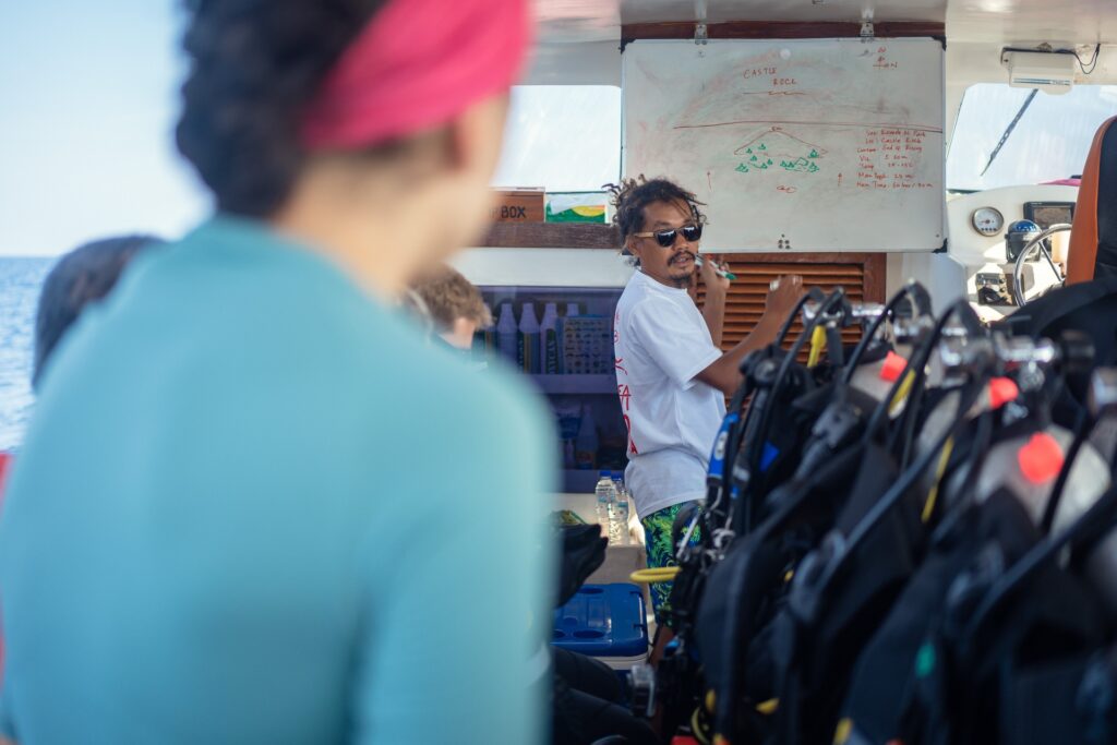 Crew member at the helm of Red Whale with dive tanks lined up on deck