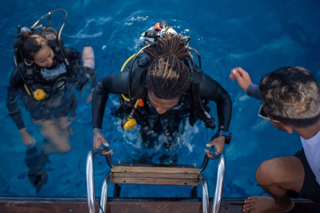 Diver climbing the boat's ladder back aboard after a dive as guests watch