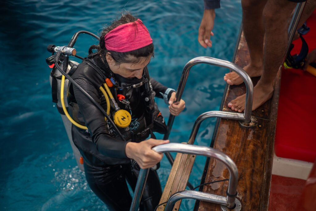 Diver in a pink headband climbing the boat's boarding ladder after a dive