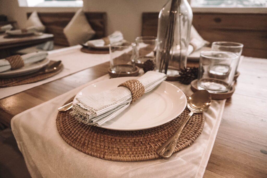 Table setting with white plate, woven rattan placemat, and cutlery on linen