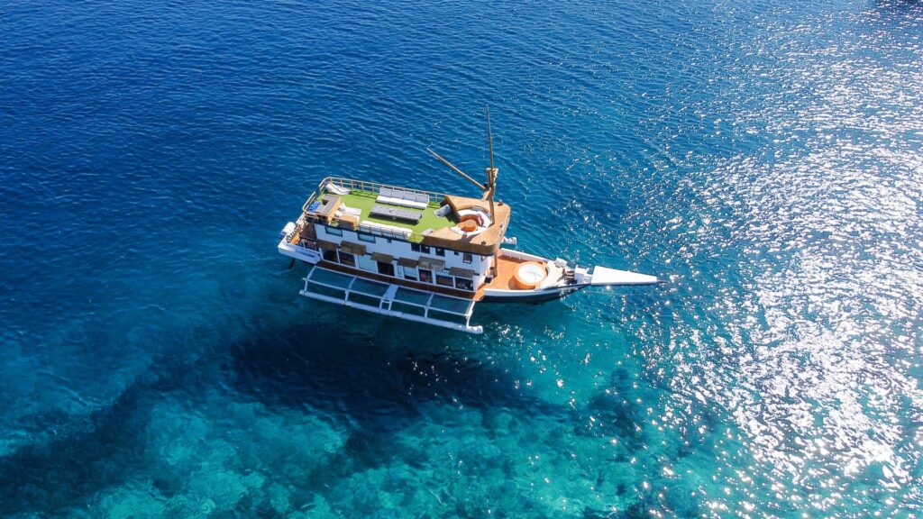 Aerial shot of a phinisi anchored in turquoise water with a green turf deck