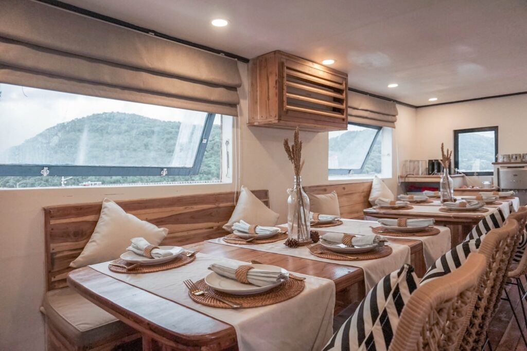 Indoor dining salon with long wooden tables and large windows looking out to green hills