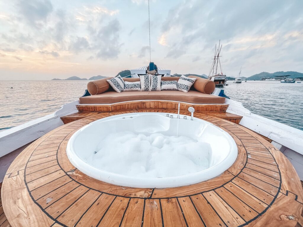 Round jacuzzi on Sea Familia's timber deck with anchored boats visible beyond