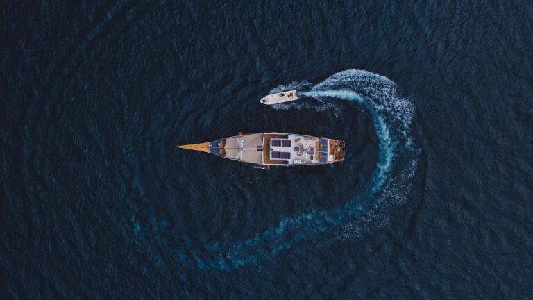 Top-down aerial of the Semesta Voyage phinisi carving a white wake across dark blue water