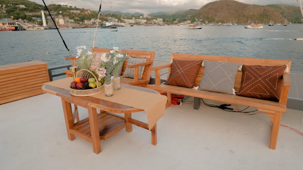 Shaded deck seating with wooden benches and a fruit basket overlooking the harbor