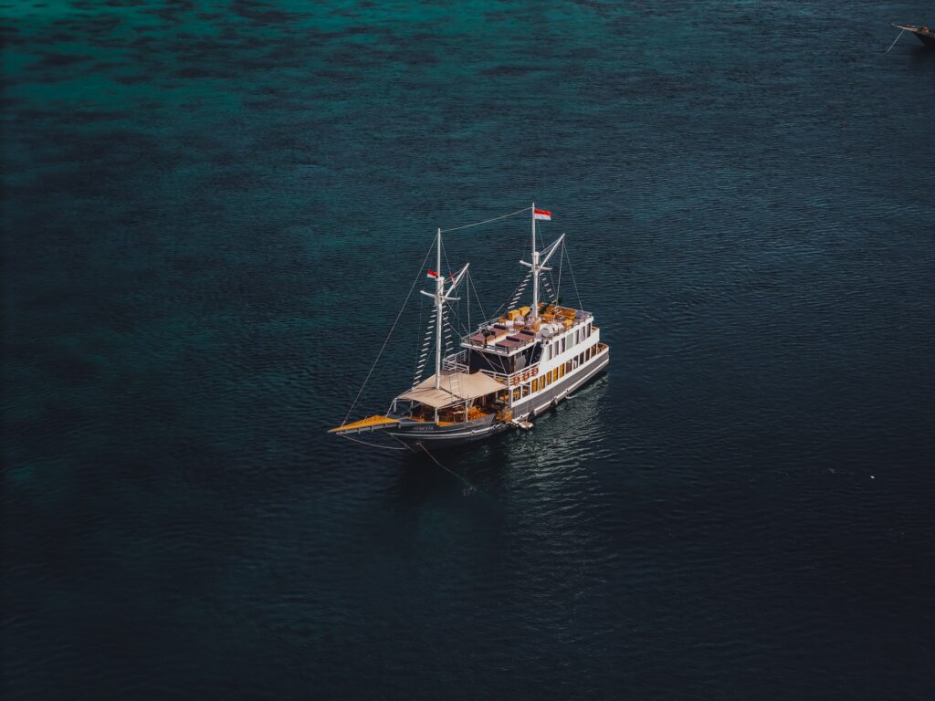 Semesta Voyage phinisi seen from a distance, anchored alone in open dark blue sea