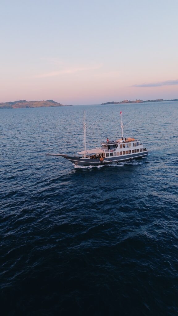 Semesta Voyage Komodo liveaboard cruising past distant islands under a soft pink sunset sky