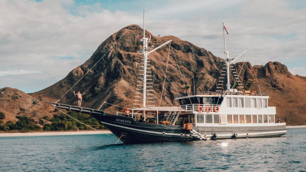 Semesta Voyage phinisi anchored near a rocky headland with clear turquoise water