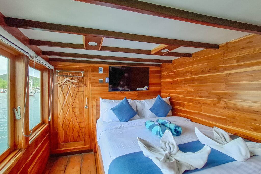 Deluxe cabin double bed with blue and white linens and ocean-view windows