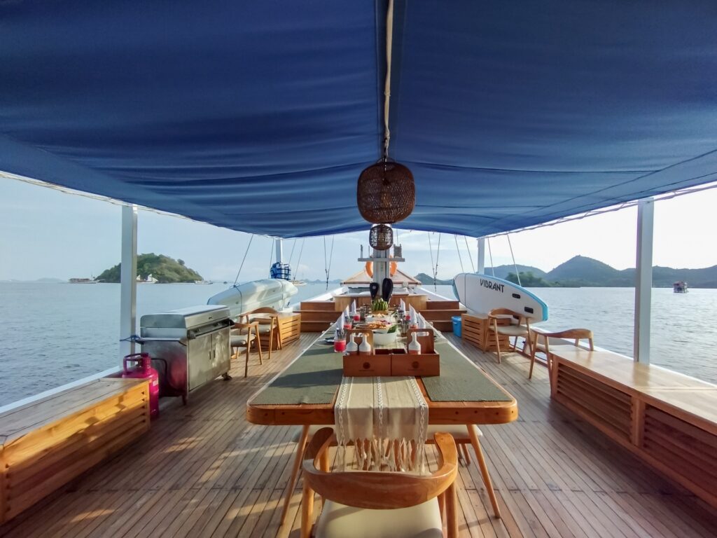 Long wooden dining table set under a blue canopy with sea views