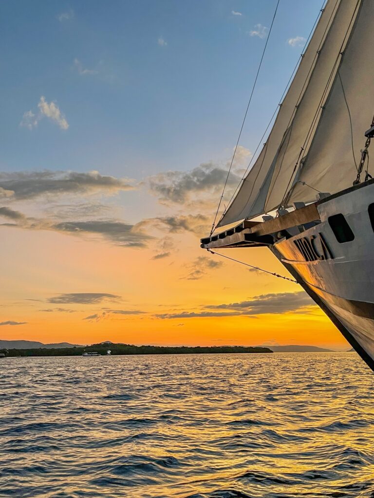Vinca Voyage's bow rising against a glowing orange sunset over the water