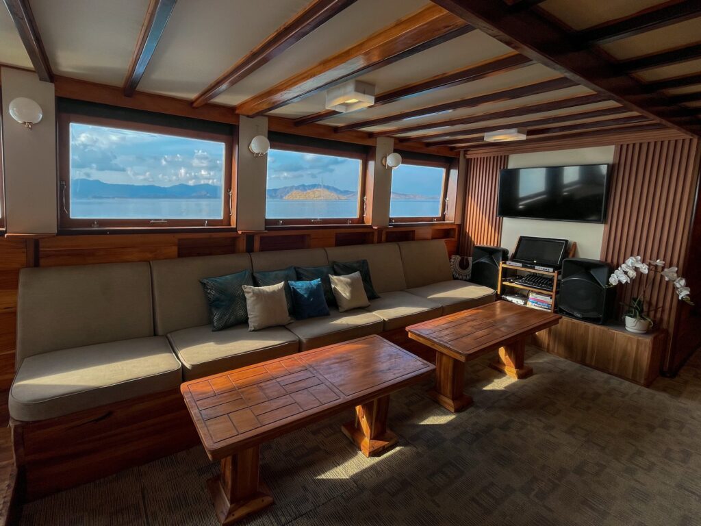 Vinca Voyage indoor salon with a long sofa, TV, and window views