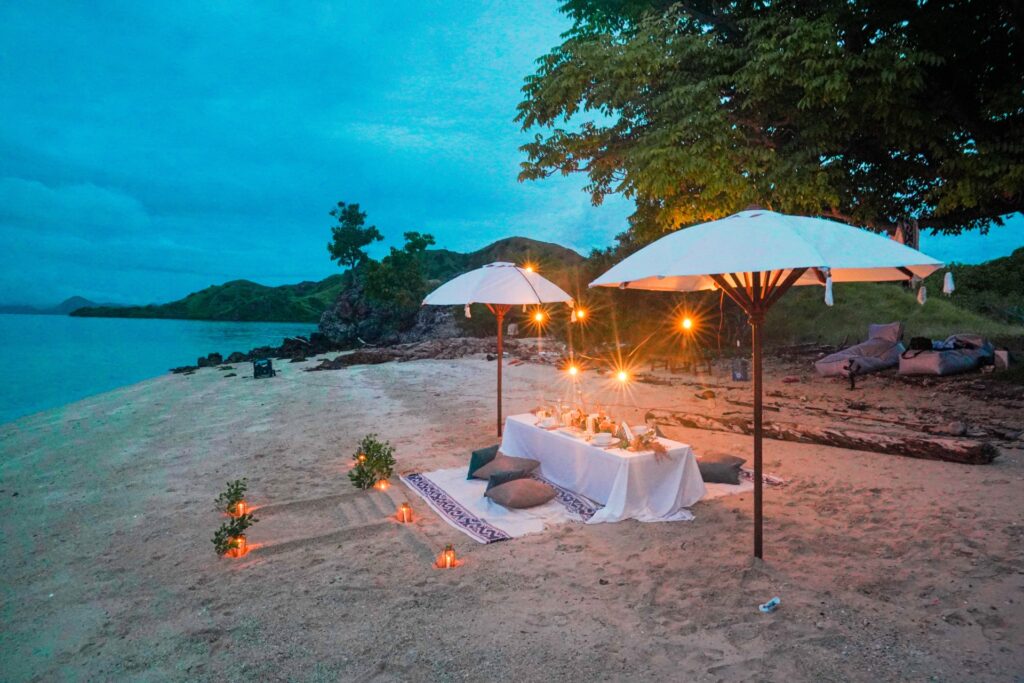 Beach dinner setup at dusk on Bidadari Island with lanterns and cushions