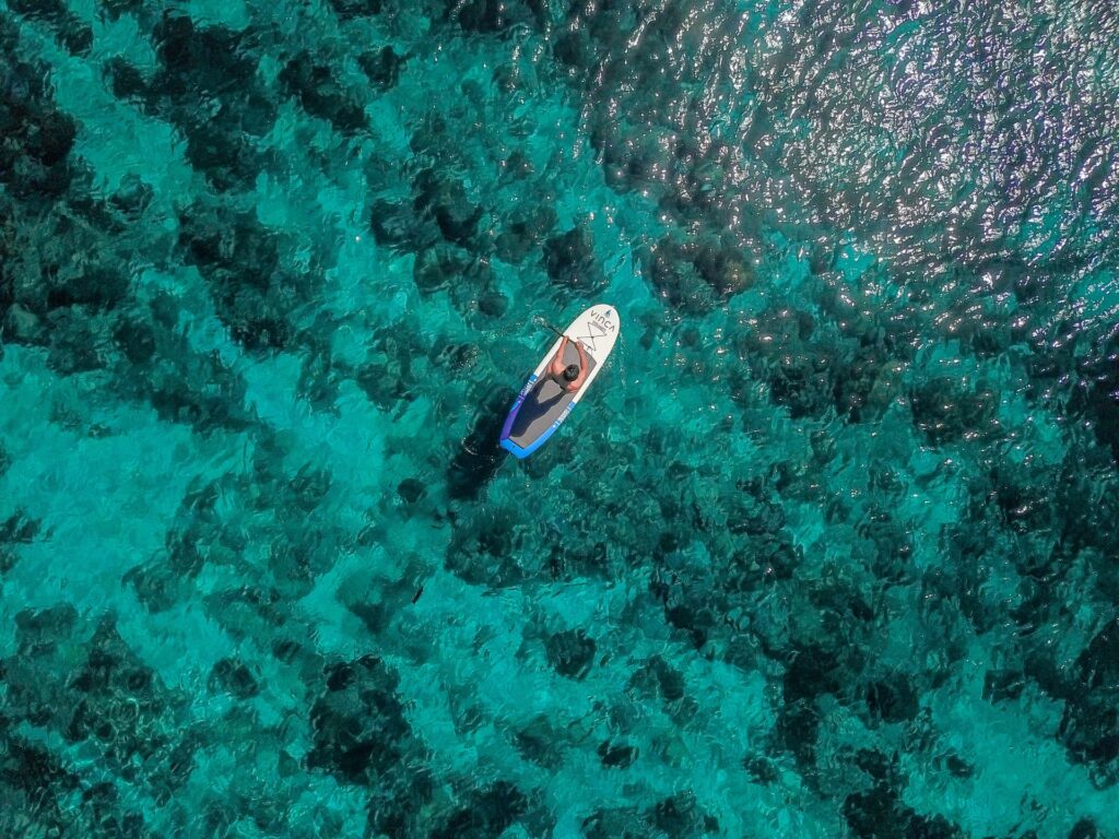 Aerial view of a guest paddleboarding over a shallow coral reef