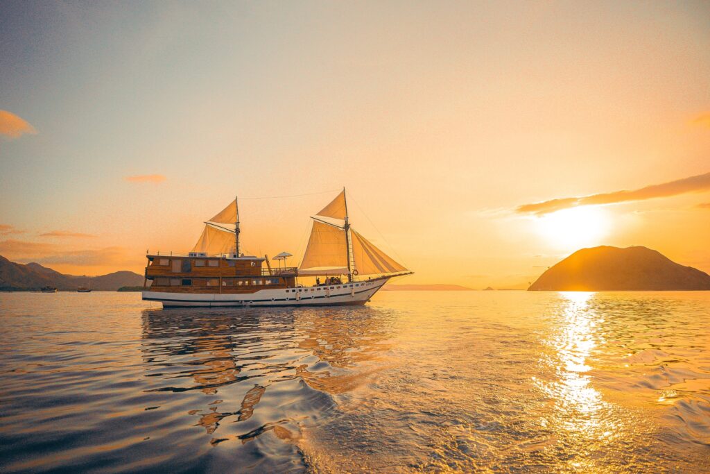 Vinca Voyage Komodo liveaboard sailing through golden hour light with sails raised